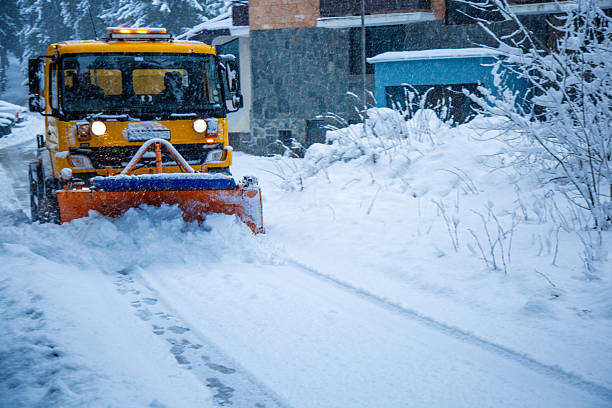 Snowplow removing accumulated snow from a road in a winter landscape during a snowfall
