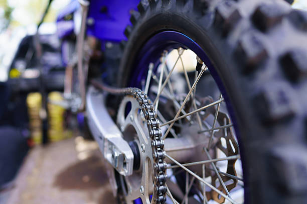 Closeup detail on rear wheel of motor dirt bike with selective focus on foreground chain area with blurred background.