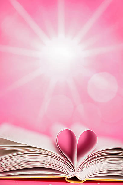 An open book with pages folded to form a heart shape. Bright sun shines in the background, creating a pink scene. The focus is on the heart and the pages. Space for copy.