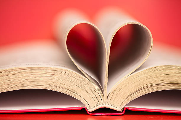 Close-up of an open book with pages folded into a heart shape. Red background, shallow depth of field.