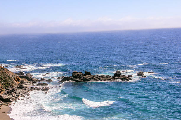 The ocean is calm and the sky is clear. The water is blue and the rocks are scattered along the shore