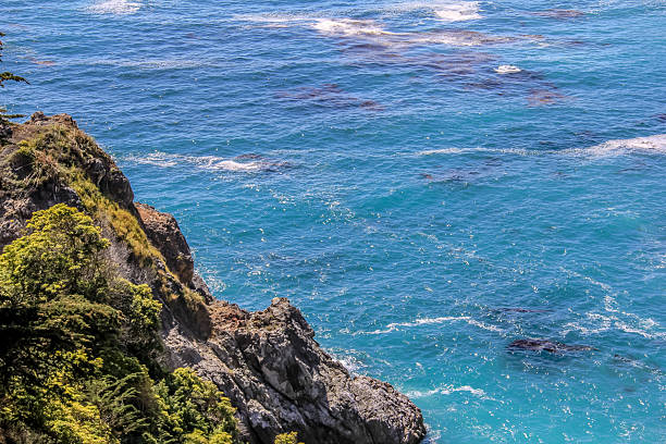 The ocean is calm and the sky is clear. The water is blue and the rocks are grey