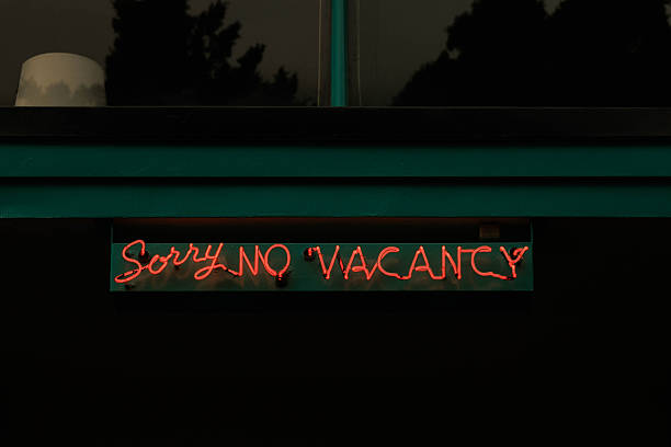 Glowing red neon 'Sorry No Vacancy' motel sign mounted beneath a teal facade, set against a dark night background to evoke nostalgia, closure, and urban roadside atmosphere.