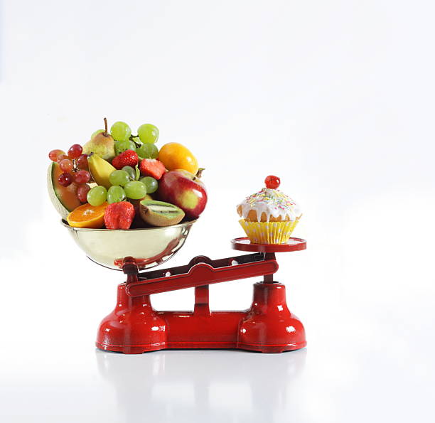 Weight scale with fresh fruit on one side and cupcake on other side, England