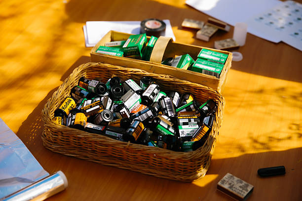 A wicker basket filled with assorted 35mm film rolls, including Kodak and Fujifilm, alongside boxed film, placed on a wooden table under sunlight. Nostalgic for analog photography