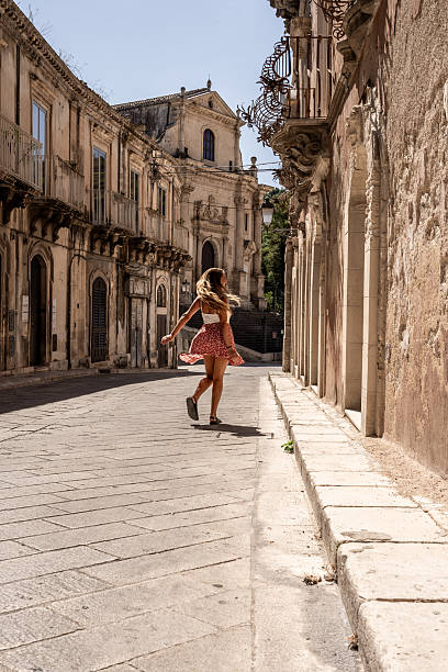 Back view of young woman spinning on sunny old town street with baroque buildings