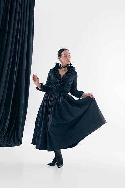 Black dress woman performing graceful studio pose with expressive confidence. Concept of timeless fashion, feminine movement, classic silhouettes, poetcore aesthetics and artistic editorial styling.