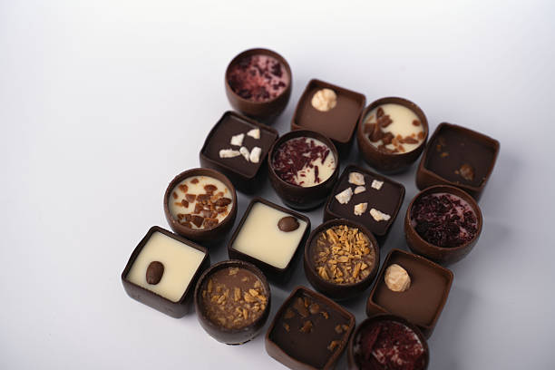 assorted gourmet chocolate bonbons and truffles artfully arranged on a white tabletop backdrop, showcasing glossy dark, milk and white fillings with nut and fruit toppings and artisanal textures