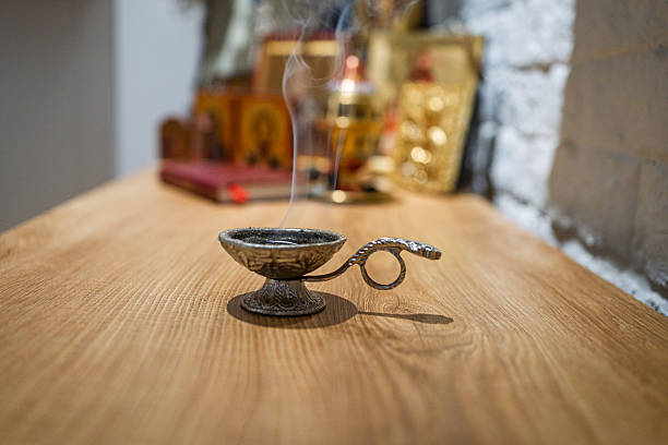 An Orthodox oil lamp, also known as a vigil lamp, is in focus, gently smoking. Blurred religious icons are visible in the background, creating a serene atmosphere.