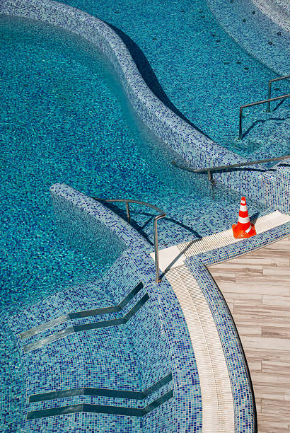 Empty swimming pool with modern design, mosaic decoration, metal handrails for safe entry into the water and clear blue water in summer. Beginning of the season