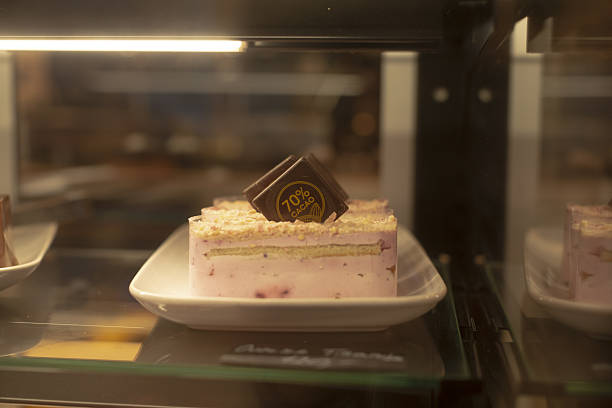 Single mousse cake plated on saucer in restaurant interior showcase, delicate emblem on glossy top, refined portion and elegant garnish under soft display lighting, boutique cafe