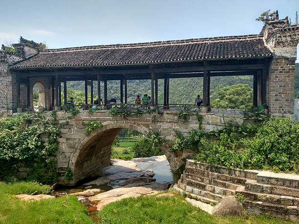 Huangmei, Hubei Province, China - August 09, 2016: The building exterior of a historical covered bridge featuring traditional stone arches and a tiled roof over a small stream in Huangmei.