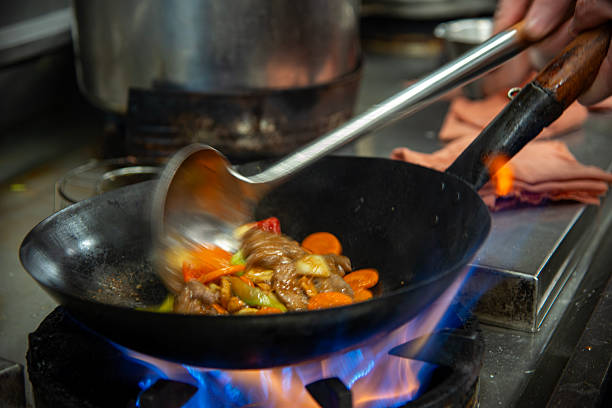 Chef in restaurant kitchen at stove with high burning flames