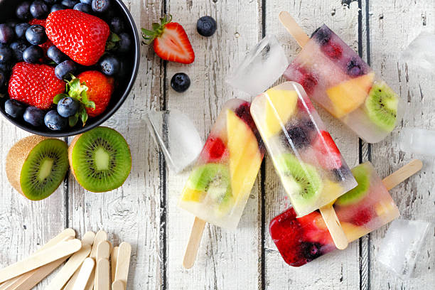 Healthy mixed fruit summer popsicles. Top view table scene on a white wood background.