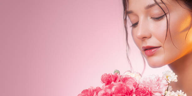 Close-up beauty profile of woman with eyes closed beside pink carnation bouquet on pastel pink background. Soft studio light and copy space, ideal for skincare ads, banners and packaging online.