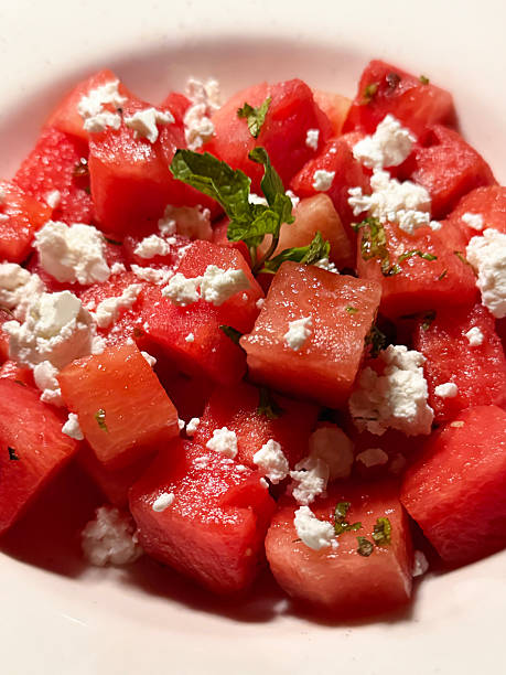 Full frame image of Greek style watermelon salad in white bowl, crumbled feta cheese, mint leaf garnish, elevated view