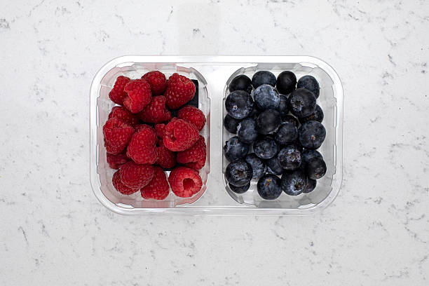 Plastic food container from a supermarket filled with raspberries and blueberries, photographed directly above