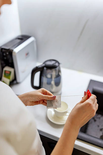 Woman Preparing Tea With Tea Bag Over Cup In Bright Kitchen Morning Routine