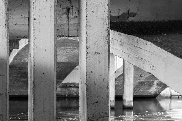 Abstract industrial background photo featuring rugged concrete pillars, a curved ramp, and stark shadows beneath a bridge. Industrial architecture template