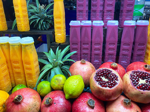 Fresh tropical fruits including pomegranates, lemons, and pineapples displayed alongside colorful juice bottles in a vibrant market setting