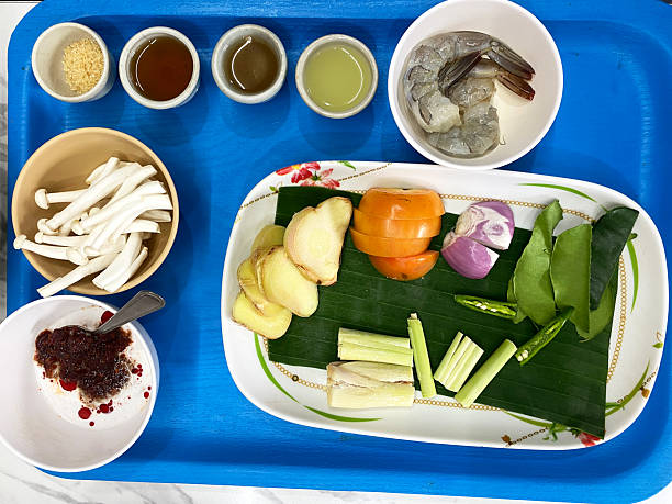 Ingredients for preparing Thai Tom Yum soup displayed on a blue tray, including shrimp, mushrooms, herbs, and spices arranged neatly for cooking