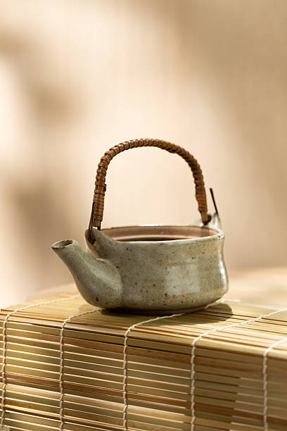 Vertical image of a traditional Japanese ceramic teapot on a bamboo mat, soft neutral tones and ample copy space above and below for branding or editorial design.