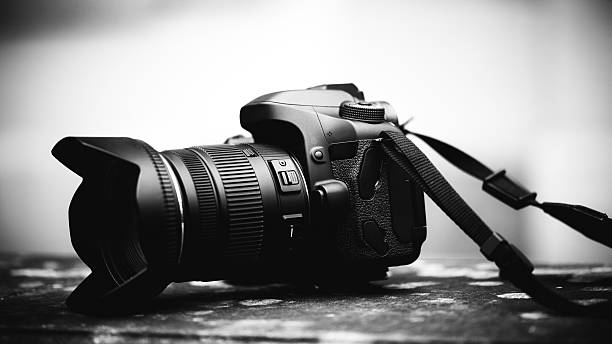 Black and white photo of a DSLR camera with zoom lens on textured surface