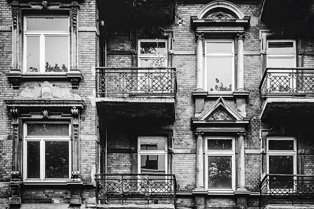 Monochrome photograph of an old brick apartment building facade with ornate balconies and windows.