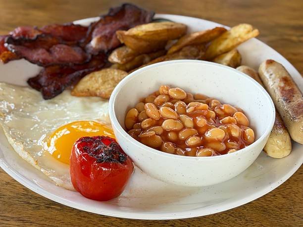 Image of top-down shot of full English fried breakfast, sizzling sausages, crispy bacon, fried eggs, grilled tomatoes, golden potato wedges, baked beans
