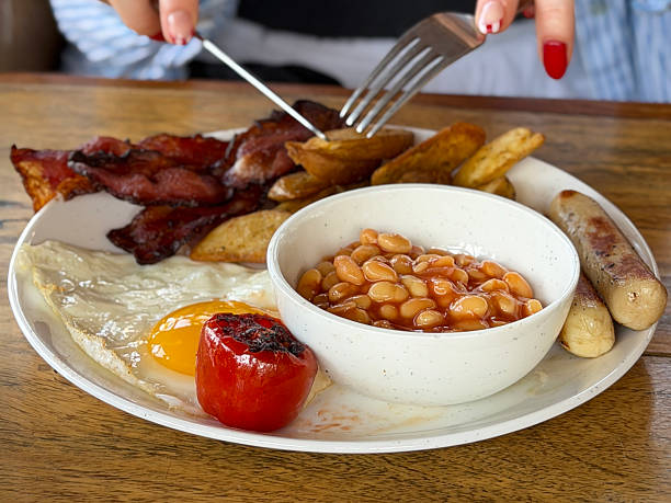 Image of full English fried breakfast with juicy sausages, crispy bacon, fried eggs, grilled tomatoes, golden potato wedges, baked beans