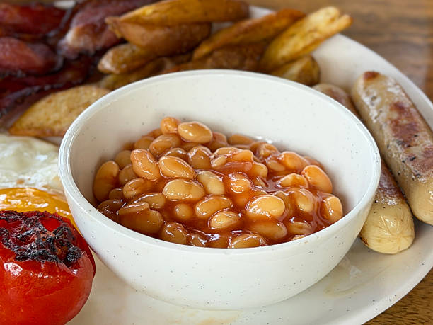 Image of a hearty full english breakfast with sizzling sausages, crispy bacon, fried eggs, grilled tomatoes, golden potato wedges