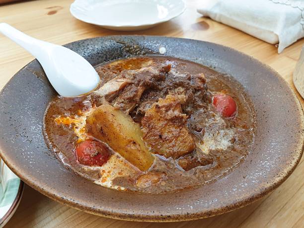 Traditional massaman beef curry with potatoes and tomatoes served in rustic ceramic bowl on wooden table for authentic asian dining experience