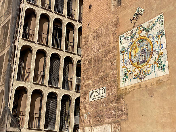 Valencia, Spain - November 12, 2023: Low angle view of mural next to directional sign pointing to a museum location. The Museo del Patriarca was founded to give access to the general public to the works belonging to the Real Colegio Seminario del Corpus Christi, located next to it.