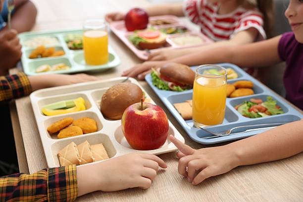 Little kids eating lunch at wooden table in school canteen, closeup