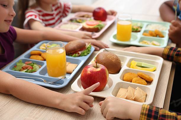 Little kids eating lunch at wooden table in school canteen, closeup