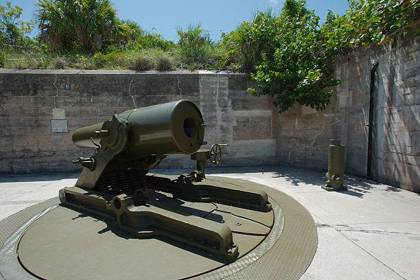 Large historic coastal mortar cannon mounted in a concrete fort battery emplacement, surrounded by weathered walls and vegetation, evoking military history, coastal defense and vintage engineering details.