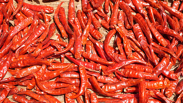 Dried red chili peppers scattered on wooden surface create vibrant and spicy visual. Their rich color and texture evoke warmth and flavor