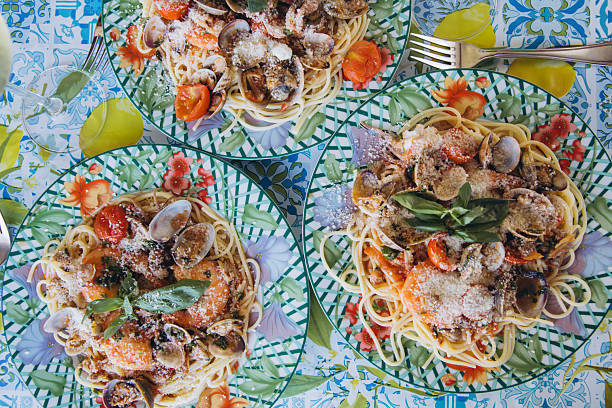 Three plates of fresh spaghetti with seafood pasta, cherry tomatoes, and basil on a colorful patterned tablecloth