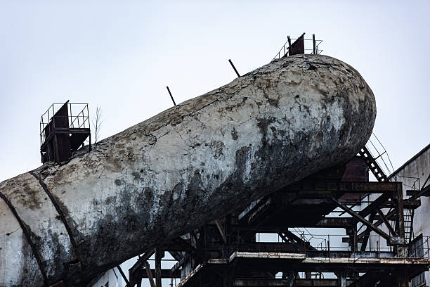 Large weathered concrete silo showing cracks and old rusty metal structure against a grey sky