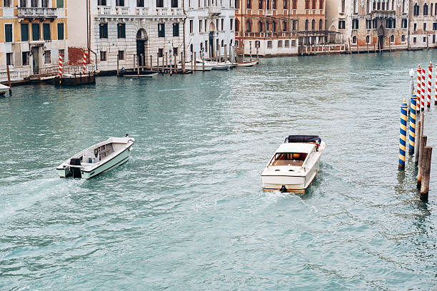 Two boats travel in a waterway in Venice with buildings in the background during the day.