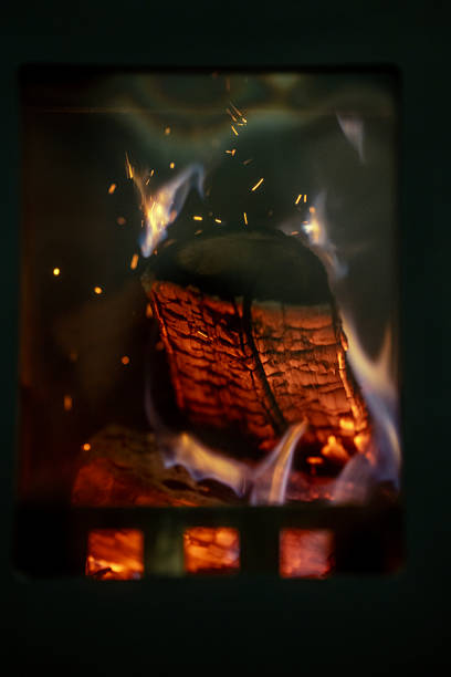 Glowing log burning inside a wood stove, emitting warm orange embers, blue flames and flying sparks; a cozy, atmospheric close-up that conveys rustic comfort, heat and the raw energy of fire.