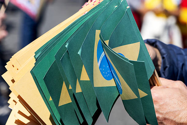 Hand holds many small Brazilian flags outdoors. Green, yellow colors with \