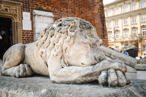 Close up of stone statue of a sleeping lion in front of the Town Hall Tower on the Main Market Square in Krakow, Poland.
