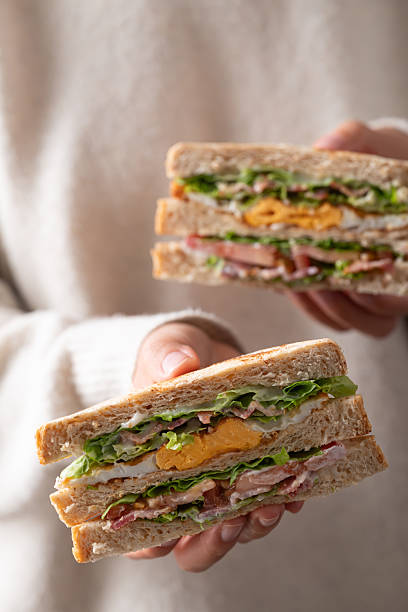 Whole wheat bread sandwich with bacon, lettuce, tomato and fried egg holding by hand