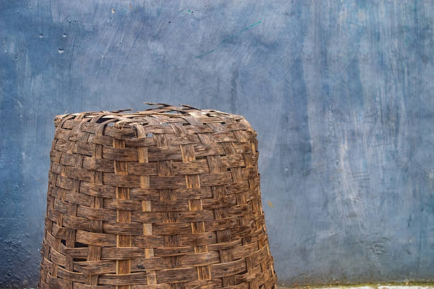 A traditional handwoven bamboo basket with a weathered texture sits in front of a textured blue wall, highlighting craftsmanship and natural materials for storage or decoration