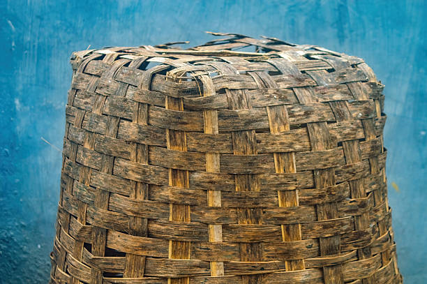 Close up of an old, weathered hand woven bamboo basket showcasing intricate weaving patterns and a rustic, textured exterior against a bright blue wall