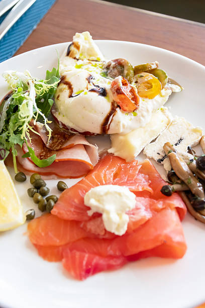 Smoked salmon and cured ham brunch plate with burrata, pickled caper, mixed greens and mushrooms, bright lemon wedge and balsamic drizzle