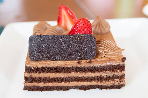 Chocolate layer cake with chocolate mousse, chocolate garnish and fresh strawberry slice, close up dessert on white plate, appetizing