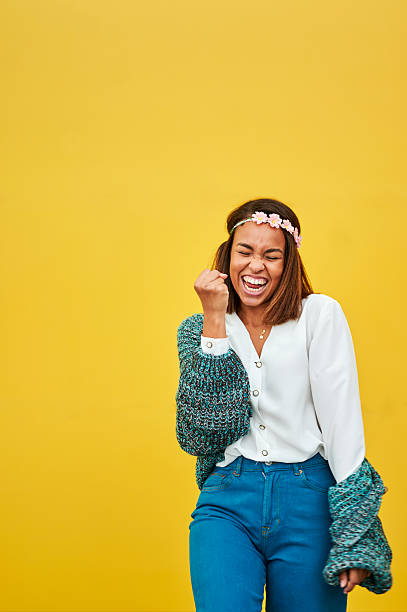 Excited young woman celebrating success with raised fist and cheerful expression on vibrant yellow background