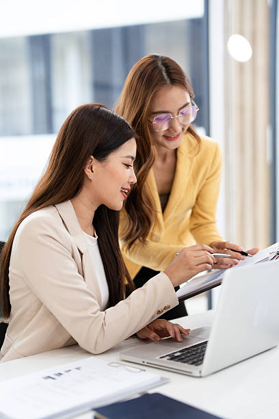 Two asian business persons working together. Businessman brainstorming, having a discussion with her colleague about work project, working on laptop computer at modern office. Business teamwork.